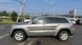 Silver SUV (Jeep Grand Cherokee) in a dealership lot with power lines overhead and an EZ Loan Auto Sales sign in the background.