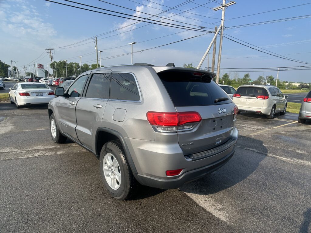 Silver Jeep SUV in a busy parking lot with other cars and overhead power lines in view.