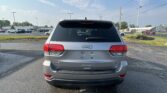 Rear view of a silver Jeep SUV in a parking lot, with the Jeep emblem on the tailgate and visible taillights under a blue sky with power lines above.