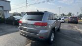 Rear view of a silver Jeep SUV in a car dealership lot with other cars and power lines overhead