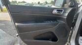 Interior of a car door panel with a chrome door handle and window controls, parking lot visible outside the window