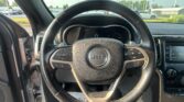 First-person view from the driver seat showing the Jeep steering wheel, dashboard, and a parking-lot scene outside the windshield