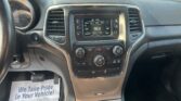 Interior view of a car dashboard with the infotainment screen, climate controls, and cup holder; a printed paper floor mat reading 'We Take Pride In Your Vehicle' is on the floor near the pedals.