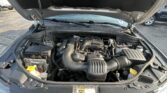 Car engine bay with the hood open, exposing the battery, air intake, and engine components in a parking lot.