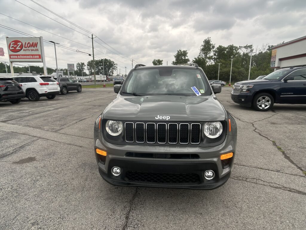 Front view of a gray Jeep SUV in a car dealership lot with other vehicles and a red E-Z LOAN sign in the background.