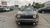 Front view of a gray Jeep SUV in a car dealership lot with other vehicles and a red E-Z LOAN sign in the background.