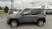 Gray Jeep Renegade SUV parked in foreground at a car dealership lot under cloudy skies, with an EZ Loan Auto Sales sign and American flag in the background.
