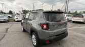 Rear three-quarter view of a gray Jeep SUV in a car dealership lot with other vehicles and a Toyota sign in the distance.