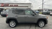 Gray Jeep Renegade SUV parked in a dealership lot with EZ LOAN AUTO SALES sign on a cloudy day.