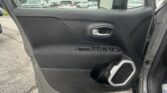 Driver-side car door interior with textured black panel, silver handle, and window controls; outside is a car dealership lot with many vehicles visible through the window.