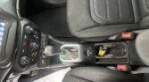 Interior view of a car's center console: gear shifter, climate control knobs, and surrounding controls, with a black seat and a red seatbelt buckle nearby.