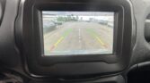 Car's dashboard screen showing the rearview backup cam view of a parking lot with green and red guiding lines and the message 'Check entire surroundings' above the image
