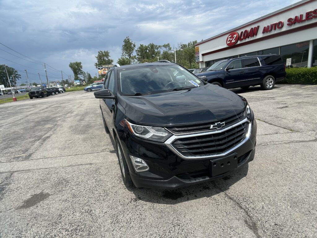 Close-up of a black Chevrolet SUV in a car lot, with an EZ Loan Auto Sales storefront in the background under a cloudy sky.