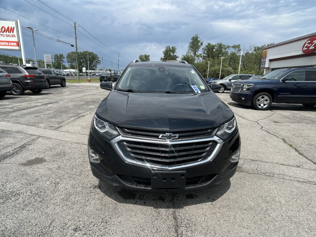 Front view of a black Chevrolet SUV parked in a lot, dealership lot with other cars and signage in the background