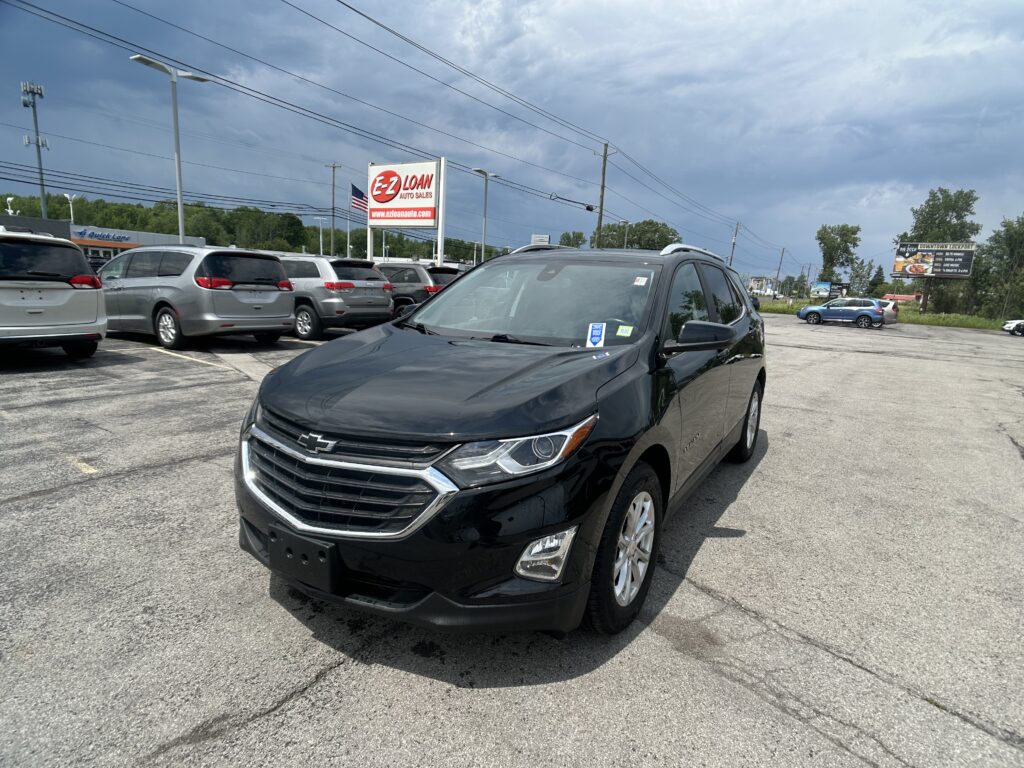 Black Chevrolet SUV in a crowded parking lot with a red EZ Auto Sales sign in the background under a cloudy sky