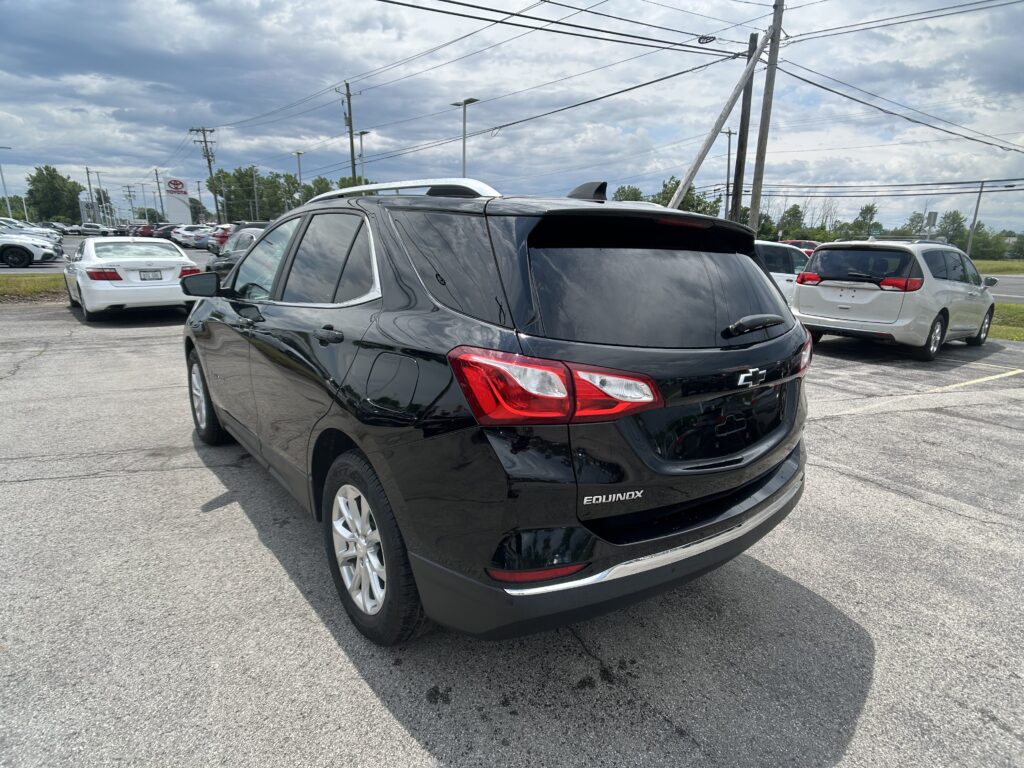 Back of a black Chevrolet Equinox in a parking lot with other cars and overhead power lines under a cloudy sky