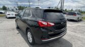 Back of a black Chevrolet Equinox in a parking lot with other cars and overhead power lines under a cloudy sky
