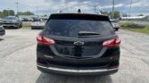 Rear view of a black Chevrolet Equinox LT in a parking lot, with other vehicles and a cloudy sky in the background