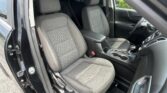 Front car interior with two black cloth seats, center console, and cup holders visible; open driver-side door with steering wheel in view.