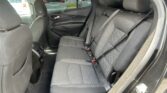 Rear passenger seating in a dark fabric SUV interior with visible seat belts and headrests; outside is a parking lot with other vehicles through the window.