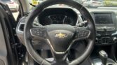 Driver's-eye view from inside a Chevrolet SUV: steering wheel centered, dashboard gauges, and infotainment screen visible with a parking lot outside the windshield.