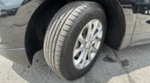 Car wheel and tire with alloy rim mounted in a black vehicle’s wheel well, parked on pavement.