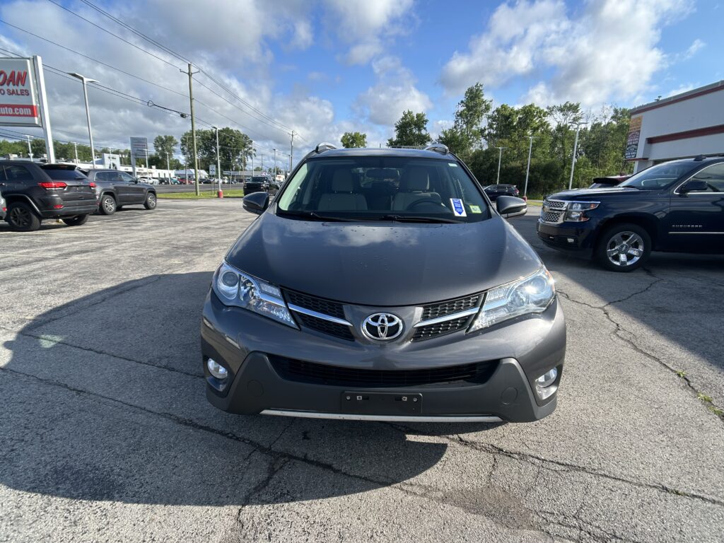 Front view of a gray Toyota SUV parked in a car dealership lot, with other vehicles and signs in the background.