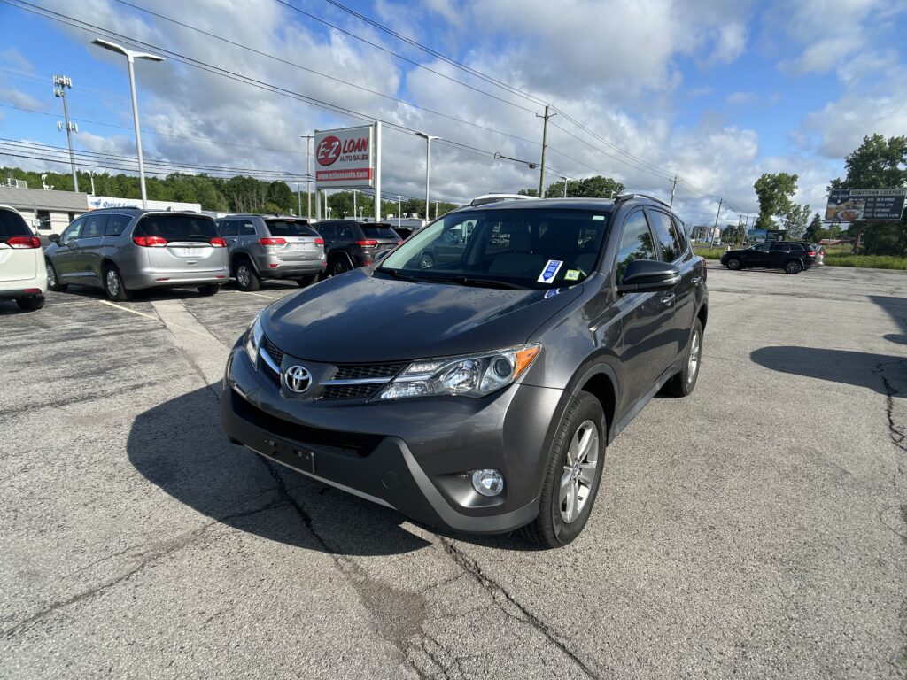 Close-up of a gray Toyota SUV in a car dealership lot with other vehicles and an EZ Loan Auto Sales sign in the background.