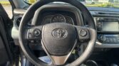Driver's-seat view of a car interior, focusing on the steering wheel with Toyota emblem and instrument cluster behind it; dashboard and center console visible.