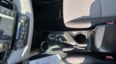 Interior of a car showing the center console with climate controls and gear selector, beige stitched seats, and cup holders.