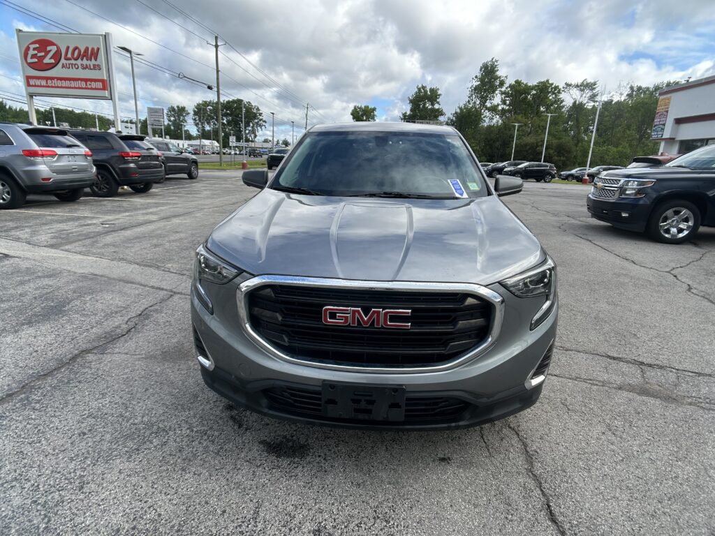 Front view of a gray GMC SUV in a car dealership lot, with other vehicles and an EZ Loan Auto Sales sign in the background.