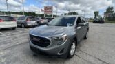 Silver GMC SUV in the foreground at an EZ Loan Auto Sales lot, with other vehicles and signs in the background under a cloudy sky.