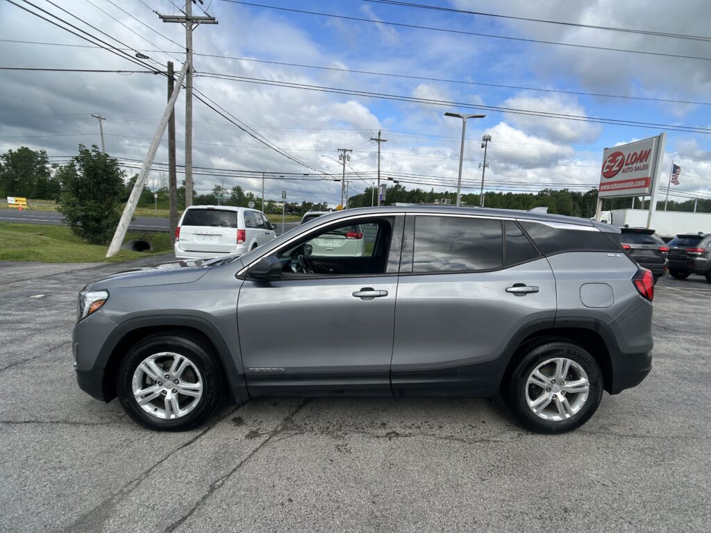 Side view of a silver GMC Terrain SUV in a dealership lot, with utility poles, power lines, and an EZ Loan Auto Sales sign in the background