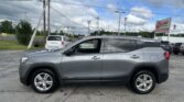 Side view of a silver GMC Terrain SUV in a dealership lot, with utility poles, power lines, and an EZ Loan Auto Sales sign in the background
