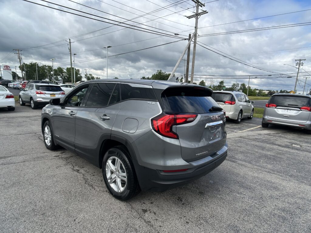 Gray GMC Terrain SUV in foreground of a car dealership lot with many parked vehicles and power lines overhead under a cloudy sky