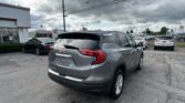 Gray GMC SUV foreground at a car dealership lot, with other cars and a Toyota dealership in the background under a cloudy sky in the distance.