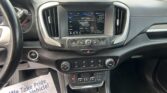 Car interior showing center touchscreen radio display (102.1 FM) with climate controls below and gear shifter nearby. A paper flyer on the floor reads 'We Take Pride In Your Vehicle'.