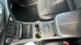 Center console of a car interior with cup holders, gear shifter, and climate controls visible beside a textured seat edge.