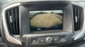 Car infotainment screen showing the rearview camera feed with yellow guide lines over a parking lot surface.