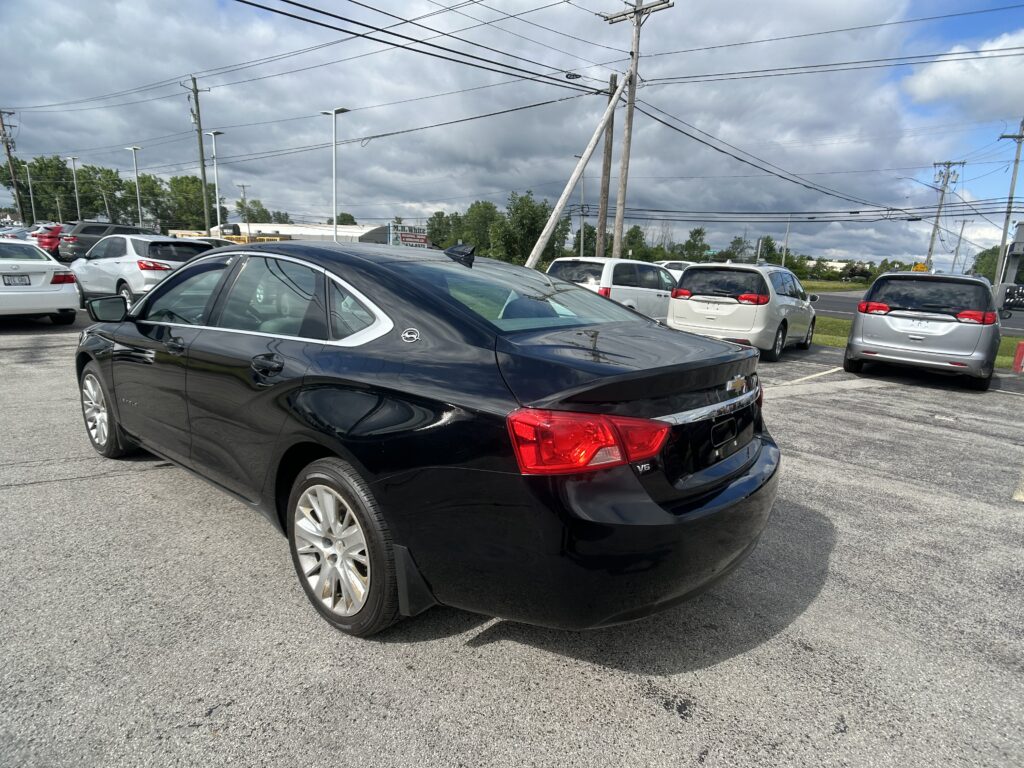Black sedan in the foreground parked in a busy parking lot with several white minivans nearby and a cloudy sky overhead.
