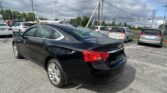 Black sedan in the foreground parked in a busy parking lot with several white minivans nearby and a cloudy sky overhead.