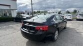 Black Chevrolet sedan in a dealership lot with other cars and a Toyota dealership building in the background under a cloudy sky.