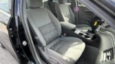 Front interior of a car showing gray fabric seats, center console, and dashboard from the driver-side door open