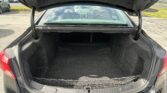 Open car trunk showing spacious empty cargo area with a black carpet and rear-view of parked cars nearby