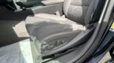 Interior of a car showing the driver seat area with a center armrest, gear shifter, and seatbelt buckle; gray fabric upholstery and sunlight on the seat.