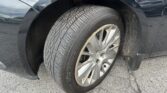 Close-up of a dark car's front wheel with a muddy tire and rust on the rim inside the wheel arch while parked on asphalt.