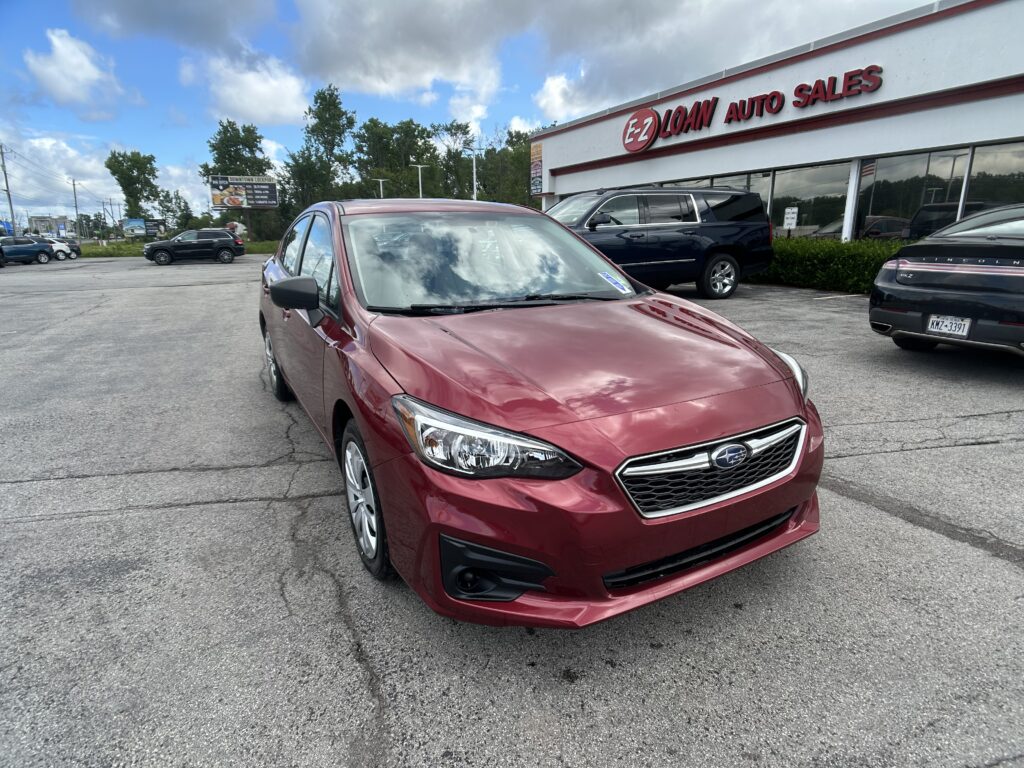 Red sedan parked in a dealership lot in front of EZ Loan Auto Sales, with other cars and a building in the background.