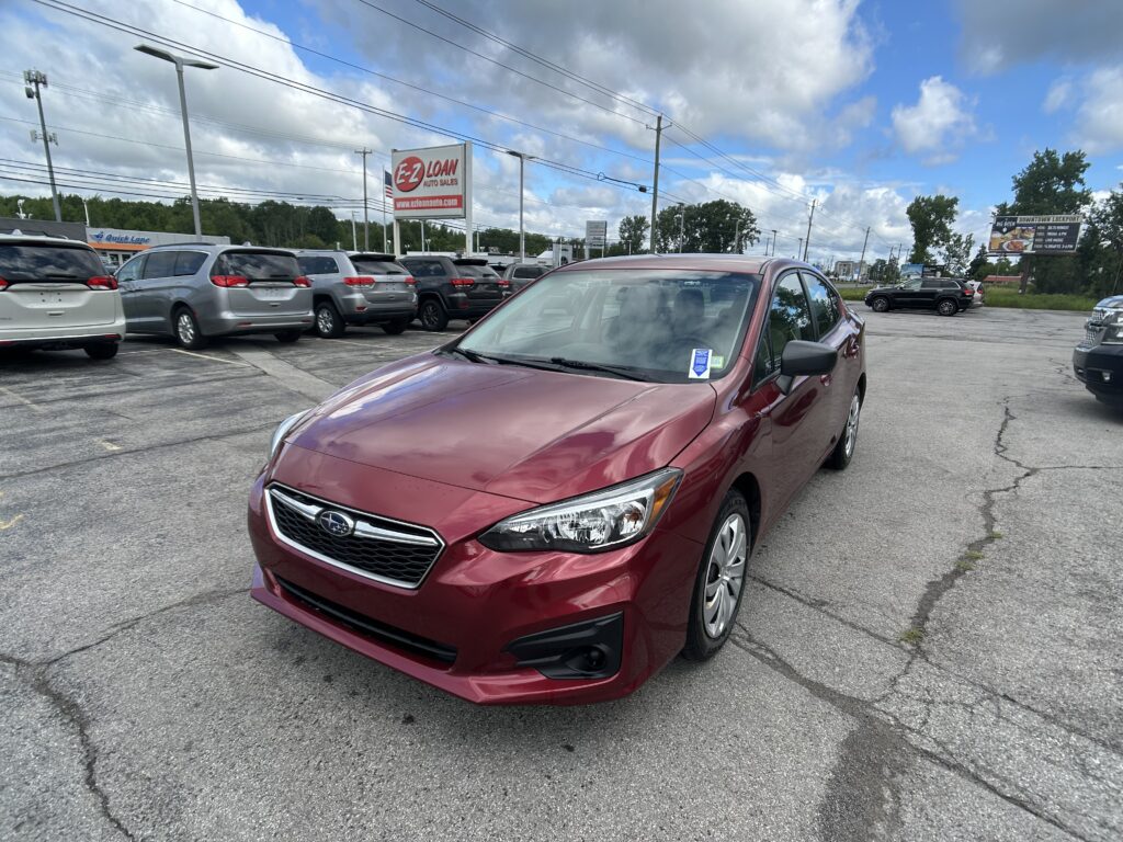 Maroon sedan in a busy parking lot with other vehicles and a roadside sign reading EZ LOAN Auto Sales in the distance.