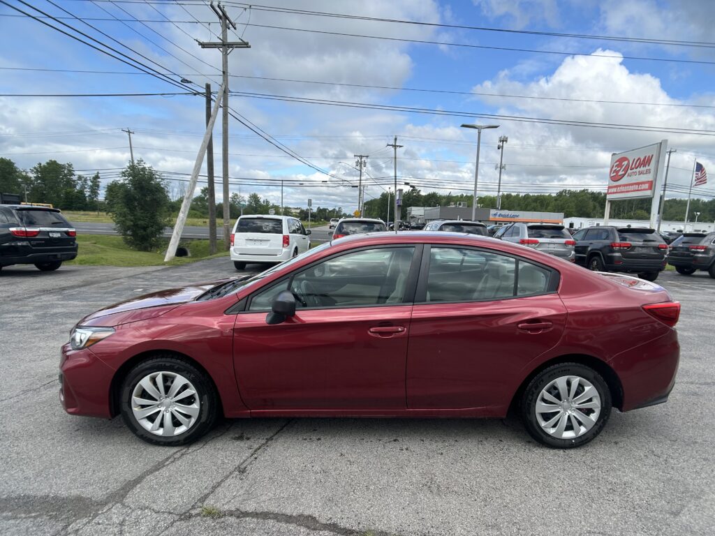 Red sedan in the foreground at a car dealership lot, with other vehicles behind it, a large EZ Loan Auto Sales sign, and power lines against a cloudy blue sky.