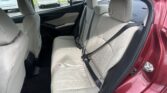 Back seat area of a red car with beige fabric upholstery and three seat belts visible behind the front seats.